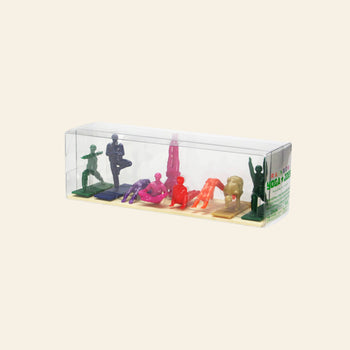 A clear plastic box displays DETAIL Yoga Joes 9 Figures—vibrant toy soldier yoga figurines by DETAIL, each in a unique pose on a small mat—set against a plain beige background.