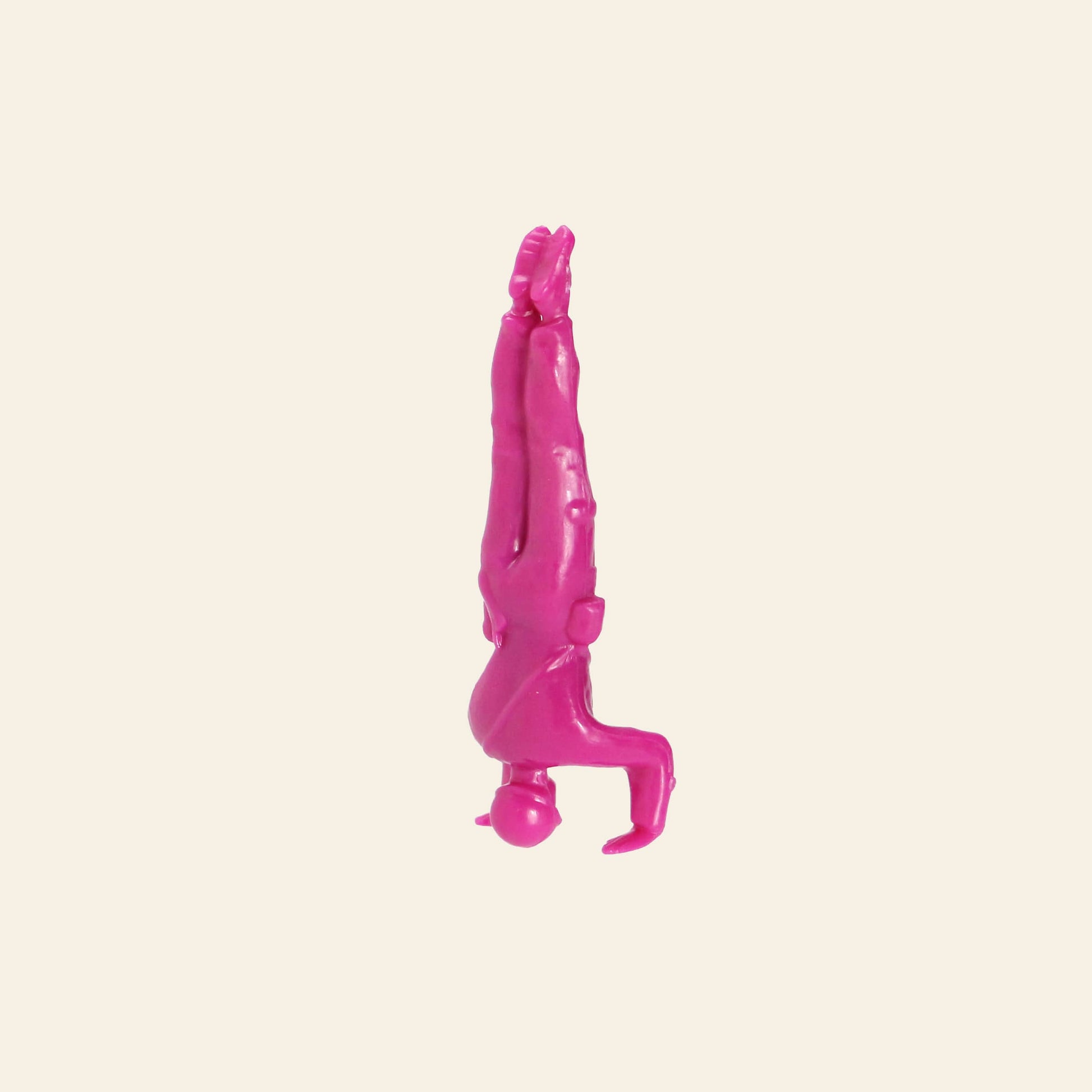 A DETAIL Yoga Joes 9 Figures pink plastic figurine from DETAIL balances on its head, legs straight up, against a plain beige background.