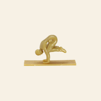 A small beige plastic yoga figurine from DETAIL Yoga Joes 9 Figures by DETAIL, showing a person balancing on their hands with one knee on an arm, posed on a rectangular base. Ideal for collectors and fans of yoga-themed toy soldiers.