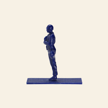 A blue plastic DETAIL Yoga Joes figure from the 9 Figures set stands upright on a rectangular base, arms bent with hands near chest, facing left against an off-white background.