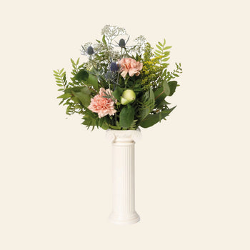 The DOIY Athena Vase by DOIY, inspired by a Greek Ionic column, displays pink carnations, green foliage, blue thistles, and yellow flowers against a plain beige background.