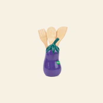 The DOIY Farmers’ Market Eggplant Utensils Pot by DOIY holds three wooden kitchen essentials—spoon and spatulas—bringing playful vegetable-themed decor to your countertop against a plain light background.