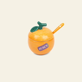 The DOIY Farmers’ Market Orange Sugar Bowl by DOIY features a ceramic orange shape with a green leaf lid, orange spoon, and purple JUICY sticker—great for sauces or dips and adding farmers market style to your table. Shown on a plain light background.