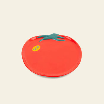 Create a unique table setting with the DOIY Farmers Market Tomato Plate by DOIY—a ceramic plate shaped like a red tomato with a green stem and yellow RIPE sticker, displayed on a light beige background.