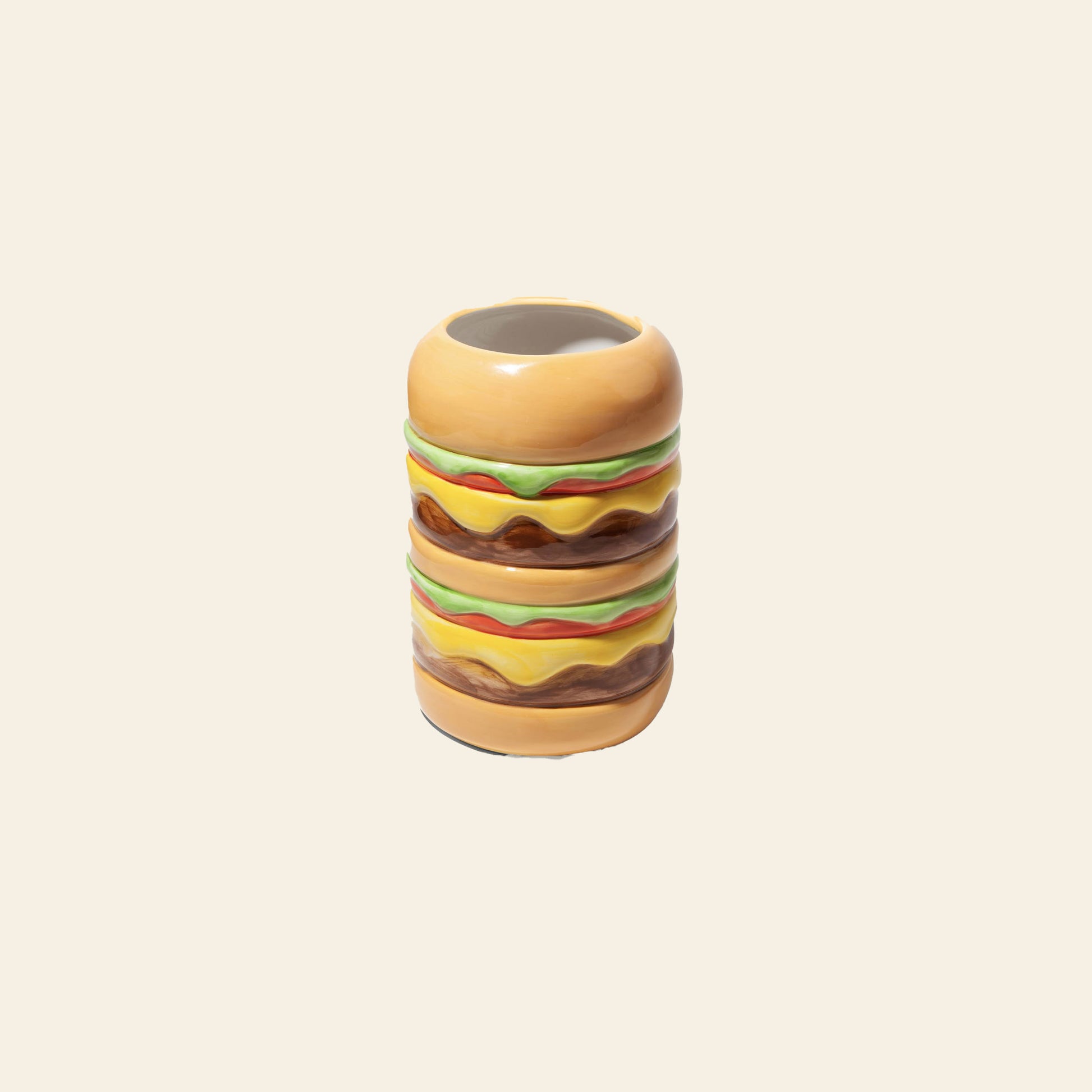 The DOIY Fast Food Burger Vase by DOIY features a retro, double cheeseburger-shaped ceramic design with buns, lettuce, cheese, and patties. Displayed on a beige background, this playful piece is part of the Fast Food Collection.