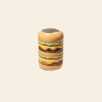 The DOIY Fast Food Burger Vase by DOIY features a retro, double cheeseburger-shaped ceramic design with buns, lettuce, cheese, and patties. Displayed on a beige background, this playful piece is part of the Fast Food Collection.