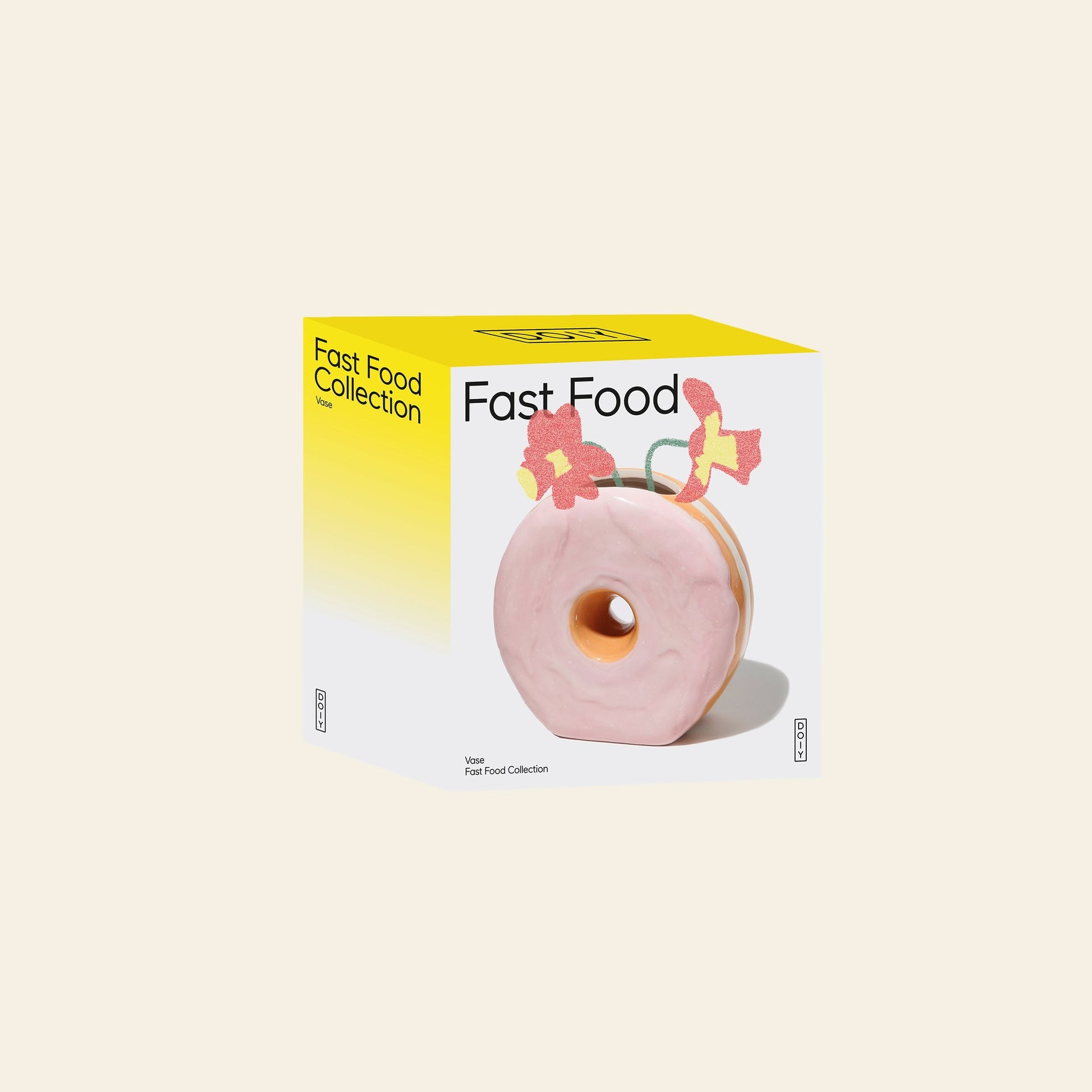 A yellow and white box labeled DOIY Fast Food Collection displays an image of the DOIY Fast Food Donut Vase, a glossy pink ceramic vase with colorful flowers on top set against a plain light background.