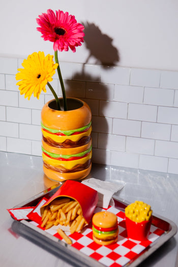 The DOIY Fast Food Fries & Burger Salt & Pepper Set features fries in a red container and a cheeseburger, displayed on a red-checkered tray, adding playful vintage charm to your decor. Brand: DOIY.
