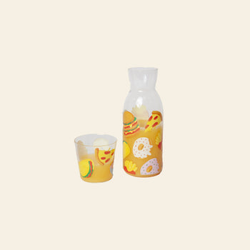 The Stacked Store DOIY Fast Food Jar & Glass Set includes a retro carafe and matching glass with colorful fast food illustrations—pizza, burgers, fries, bagels—on clear glass and a plain light background.