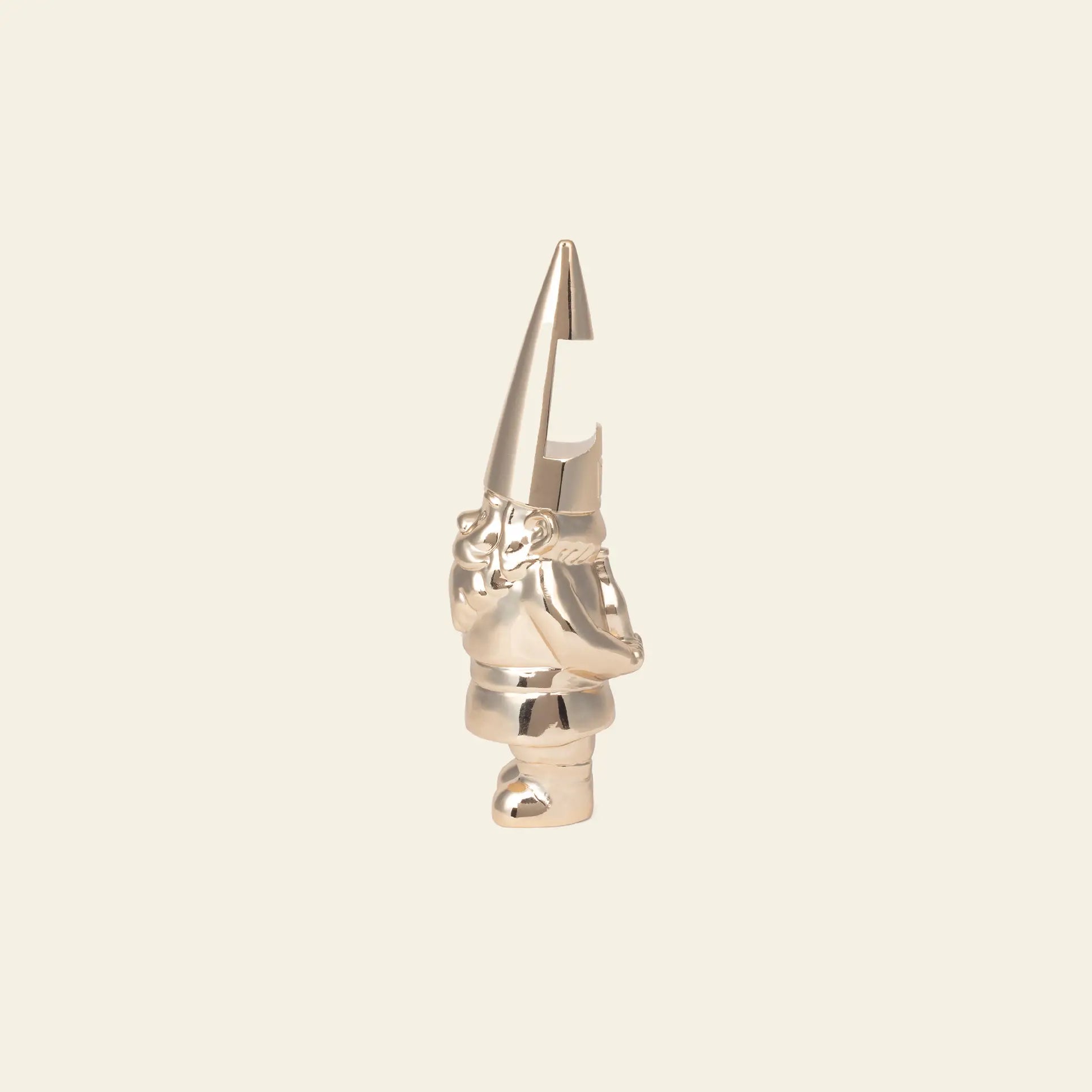 The DOIY Gnome Bottle Opener by DOIY is a metallic, shiny figurine with a tall pointed hat and crossed arms. Its hat features a carved notch at the top, perfect for opening your favorite bottles. Stands on a plain beige background.