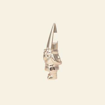 The DOIY Gnome Bottle Opener by DOIY is a metallic, shiny figurine with a tall pointed hat and crossed arms. Its hat features a carved notch at the top, perfect for opening your favorite bottles. Stands on a plain beige background.