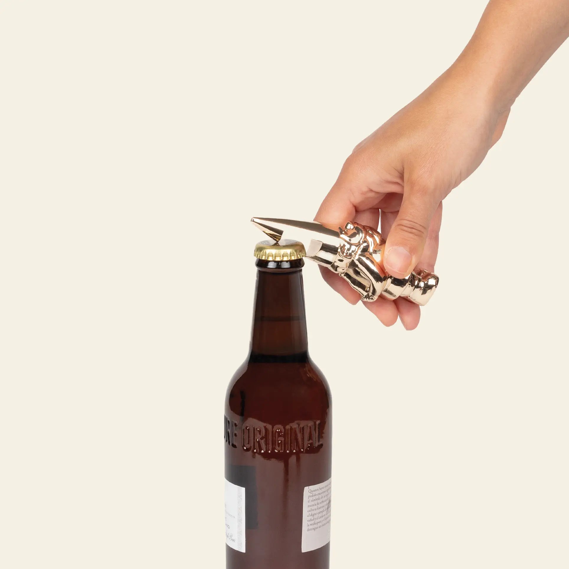 A hand opens a brown glass bottle with the DOIY Gnome Bottle Opener by DOIY, featuring a whimsical gnome fist design, set against a plain light background.