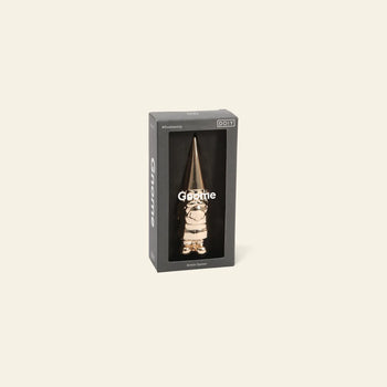 A boxed DOIY Gnome Bottle Opener in gold is visible through a clear window on black packaging labeled Gnome and DOIY, standing against a plain light background.