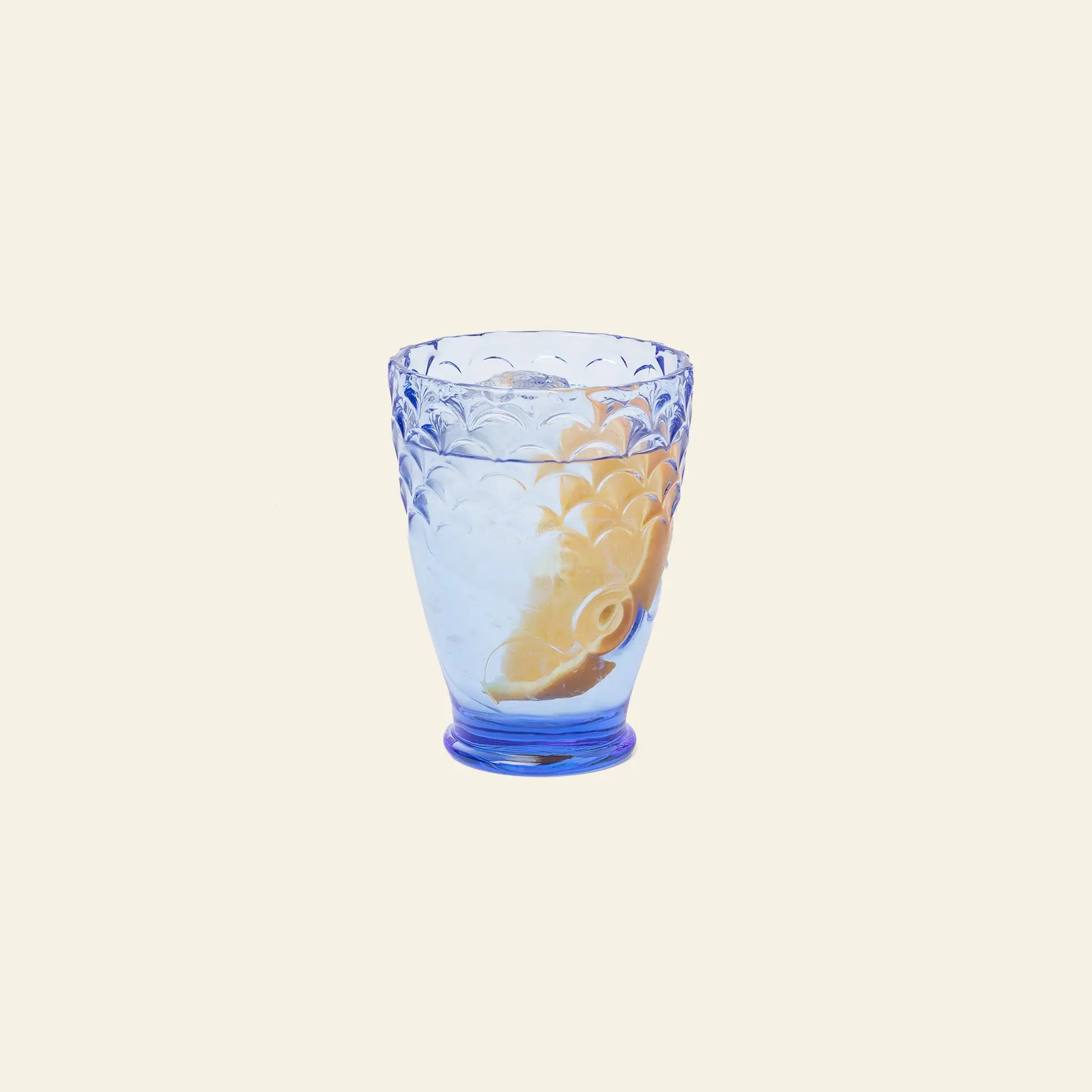 A DOIY Koifish Glass from the DOIY Koifish Glasses Set of 4, featuring a blue artistic textured design, is filled with water and a lemon wedge and set against a plain light beige background.