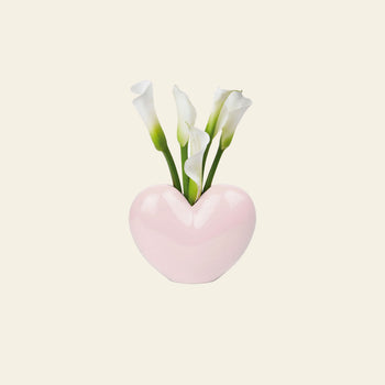 The DOIY Love Vase by DOIY features a pink, heart-shaped design holding white calla lilies with green stems, set against a light background—highlighting its sentimental style and elegant beauty.