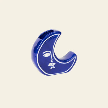 The DOIY Moon Vase by DOIY is a blue crescent-shaped ceramic vase, featuring a minimalist white line face design, shown against a plain beige background.