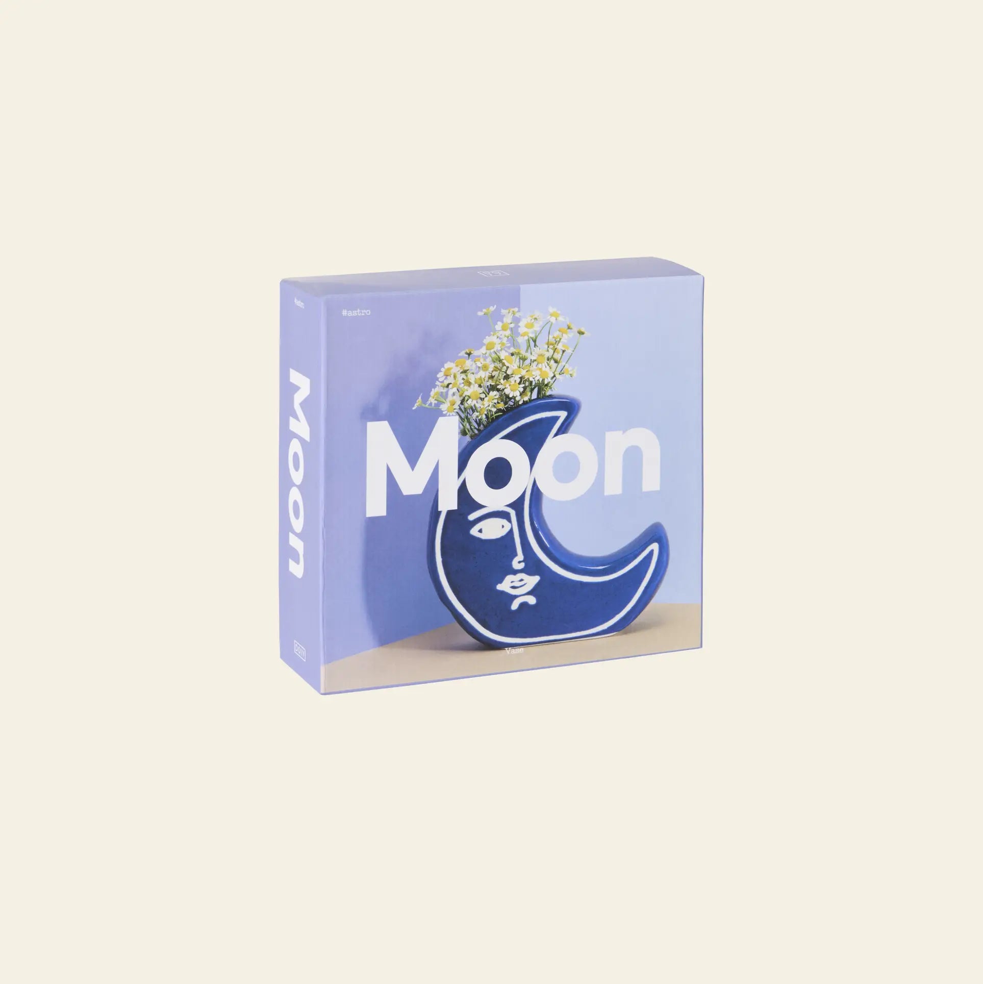 The DOIY Moon Vase by DOIY is a celestial-inspired blue crescent moon vase with a face design, holding small white flowers, displayed against a light background on the product box.