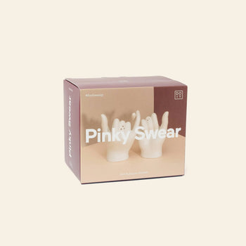The DOIY Pinky Swear Salt and Pepper Set by DOIY features two white ceramic hand-shaped shakers with interlocked pinky fingers, packaged in a contemporary box against a beige background.