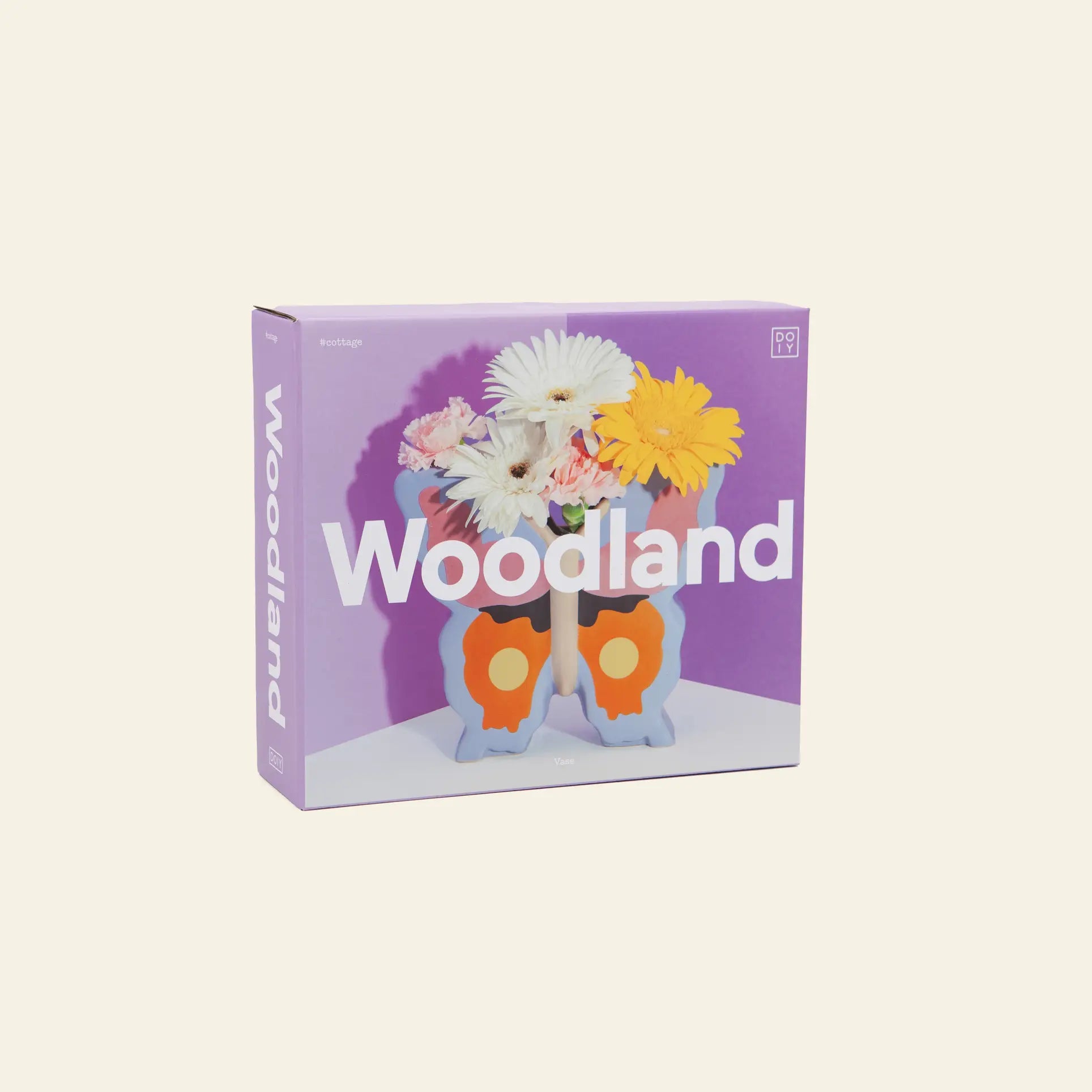 The DOIY Woodland Butterfly Vase by DOIY features a ceramic vase shaped like two cartoon mushrooms with assorted flowers, creating a charming cottage vibe against a purple backdrop.