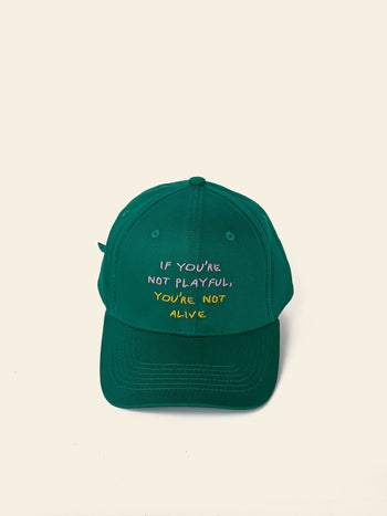 The David Hockney If You’re Not Playful Cap by David Hockney is a green cotton cap featuring the phrase “IF YOU’RE NOT PLAYFUL, YOU’RE NOT ALIVE” embroidered in colorful letters on the front, shown against a simple light background.