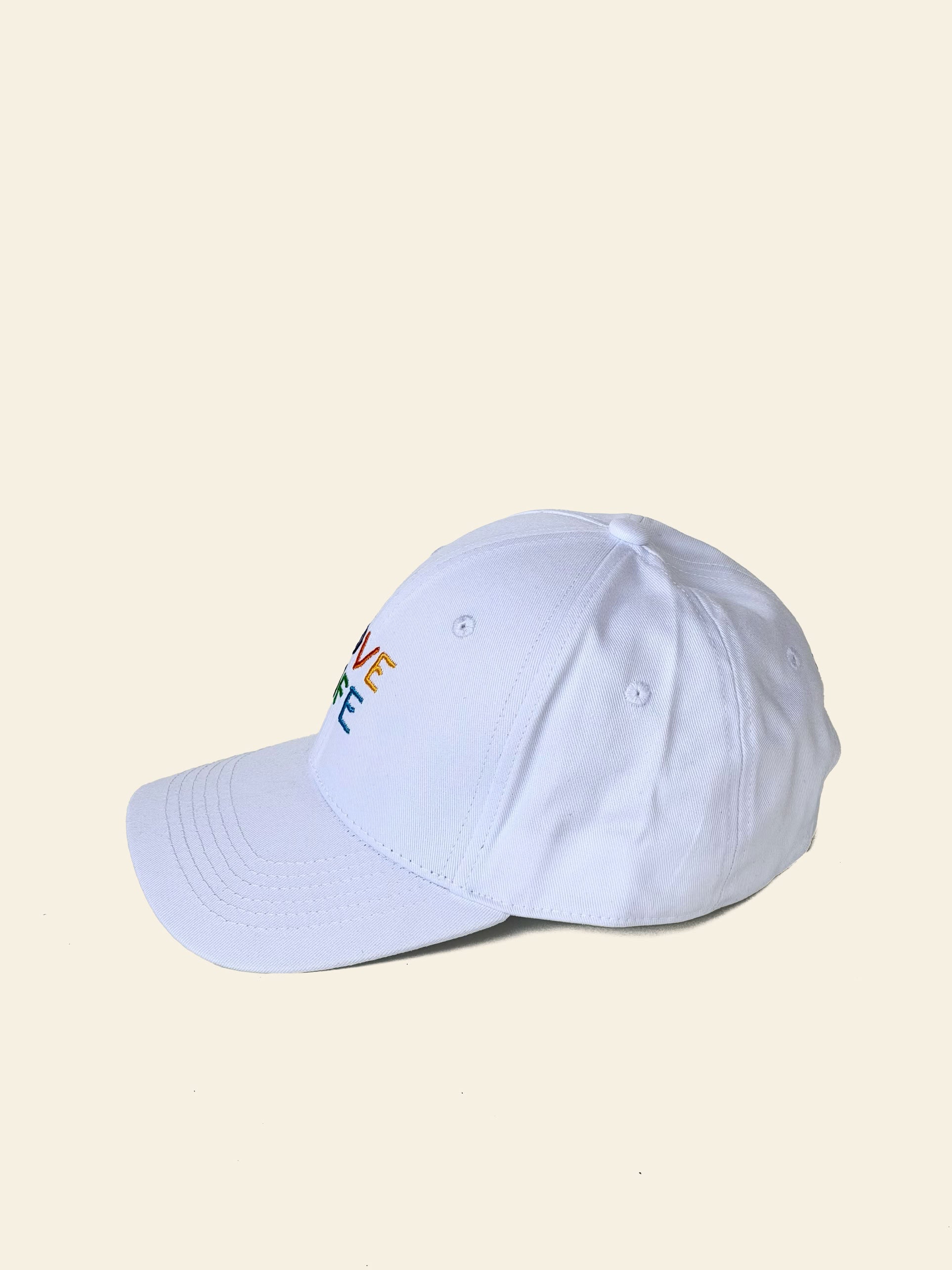 The David Hockney Love Life Cap by David Hockney is a white cotton cap featuring partially visible, colorful embroidered text on the front, photographed against a plain light background.