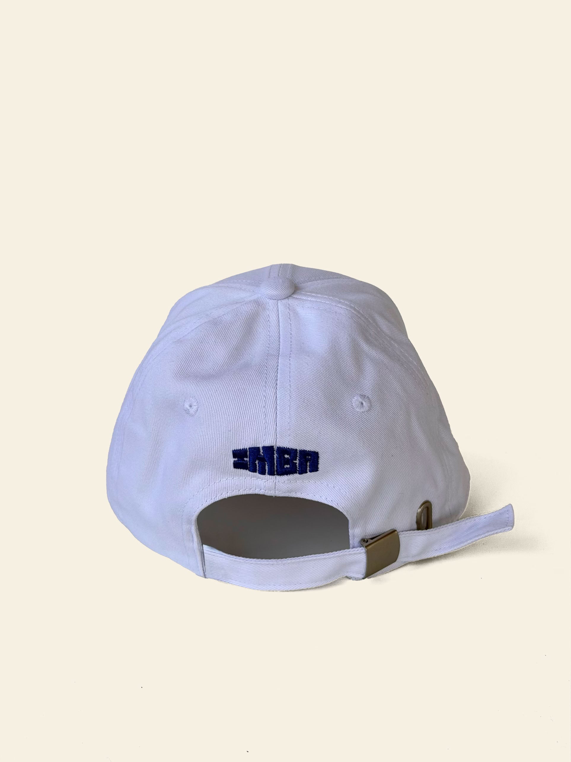 A white cotton David Hockney Love Life Cap by David Hockney, shown from the back with blue embroidered text above the adjustable strap and metal buckle—perfect for fans of the classic David Hockney cap style.