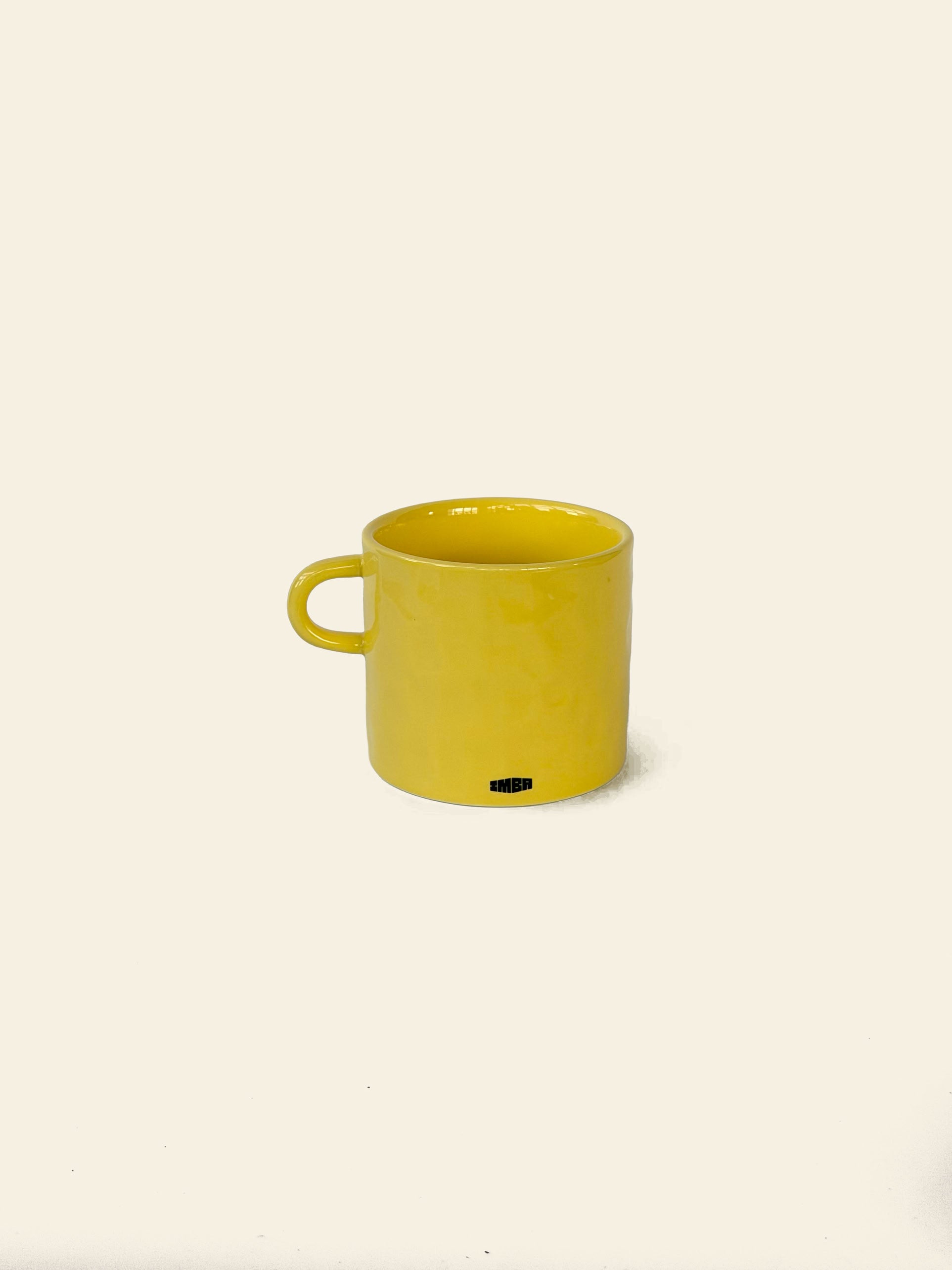 A bright yellow ceramic mug with a handle sits on a plain, light background. The David Hockney Bigger & Closer Mug by David Hockney features a subtle shine and a small black logo near its base, echoing the iconic style of Hockney’s work.