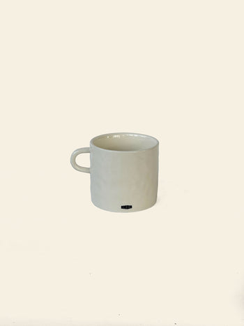 A plain white ceramic David Hockney Love Love Mug with a handle rests on a light, neutral background. The mug features a subtle textured surface and a small black David Hockney logo near its base, embodying the minimalist elegance characteristic of the brand’s signature style.