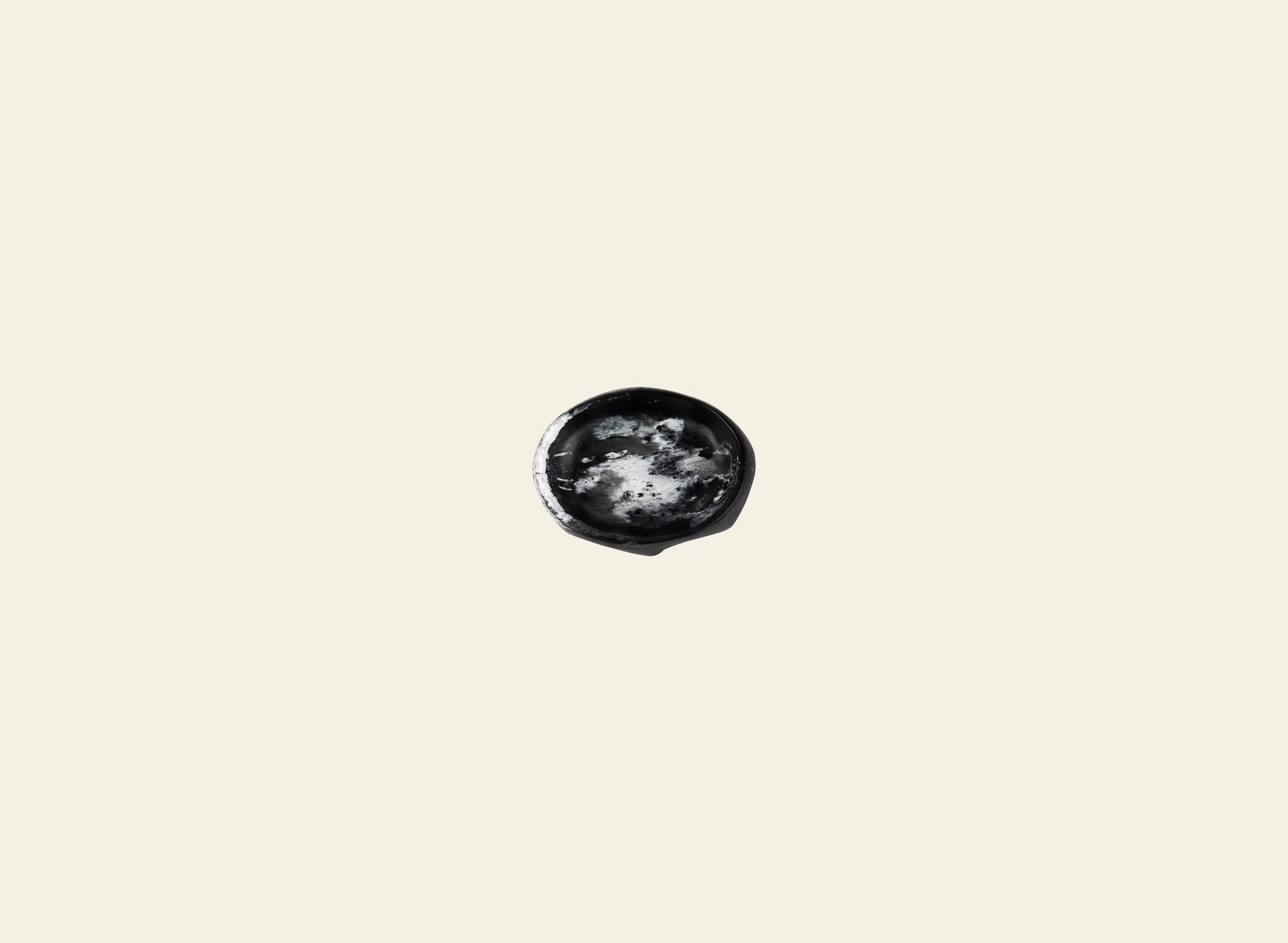 A small, dark, marbled Crown Dish by Dinosaur Designs sits centered on a plain off-white background, showcasing the sculptural aesthetic for which the brand is known.