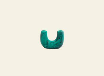 A single pink flower in a green Dinosaur Designs Mini Branch Vase from the Branch collection, inspired by Stephen Ormandy, sits on magazines—including LIGURIA—atop a light wooden surface against a gray wall.