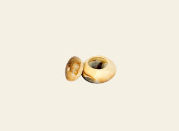 A handmade Dinosaur Designs Small Pebble Jar with a matching lid, both featuring natural beige and brown marbled patterns, is displayed against a plain light background.