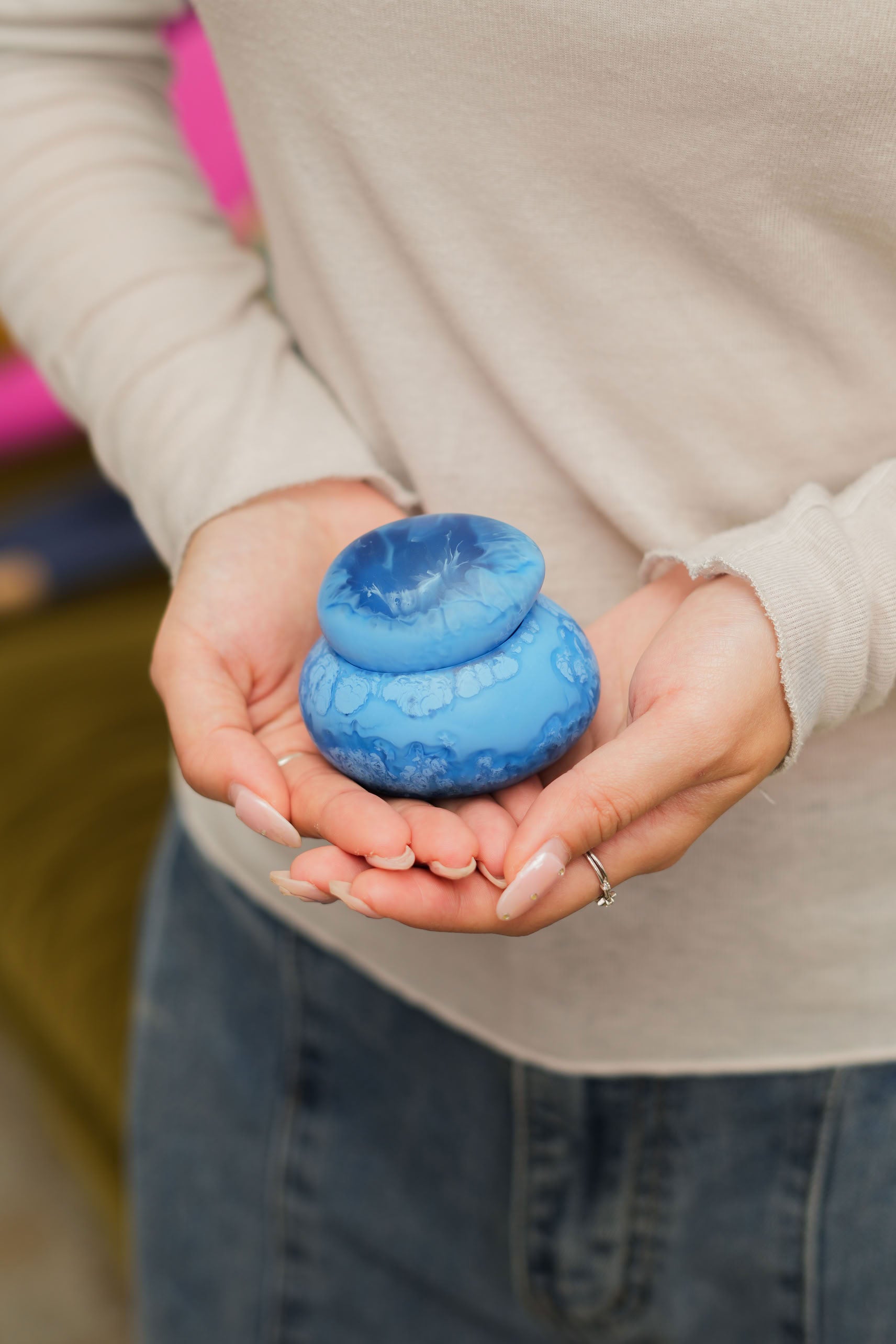 A person in a light long-sleeve shirt and jeans holds the Dinosaur Designs Small Pebble Jar, featuring a versatile lid, in both hands.