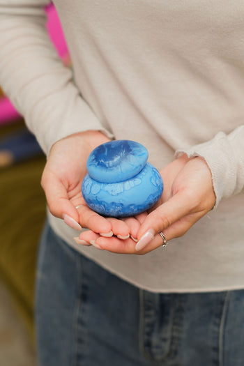 A person in a light long-sleeve shirt and jeans holds the Dinosaur Designs Small Pebble Jar, featuring a versatile lid, in both hands.