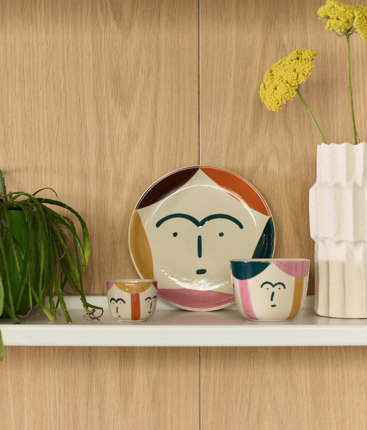 The Donna Wilson Freya Face Cup by Donna Wilson sits on the shelf, highlighting the charm of hand-painted stoneware.