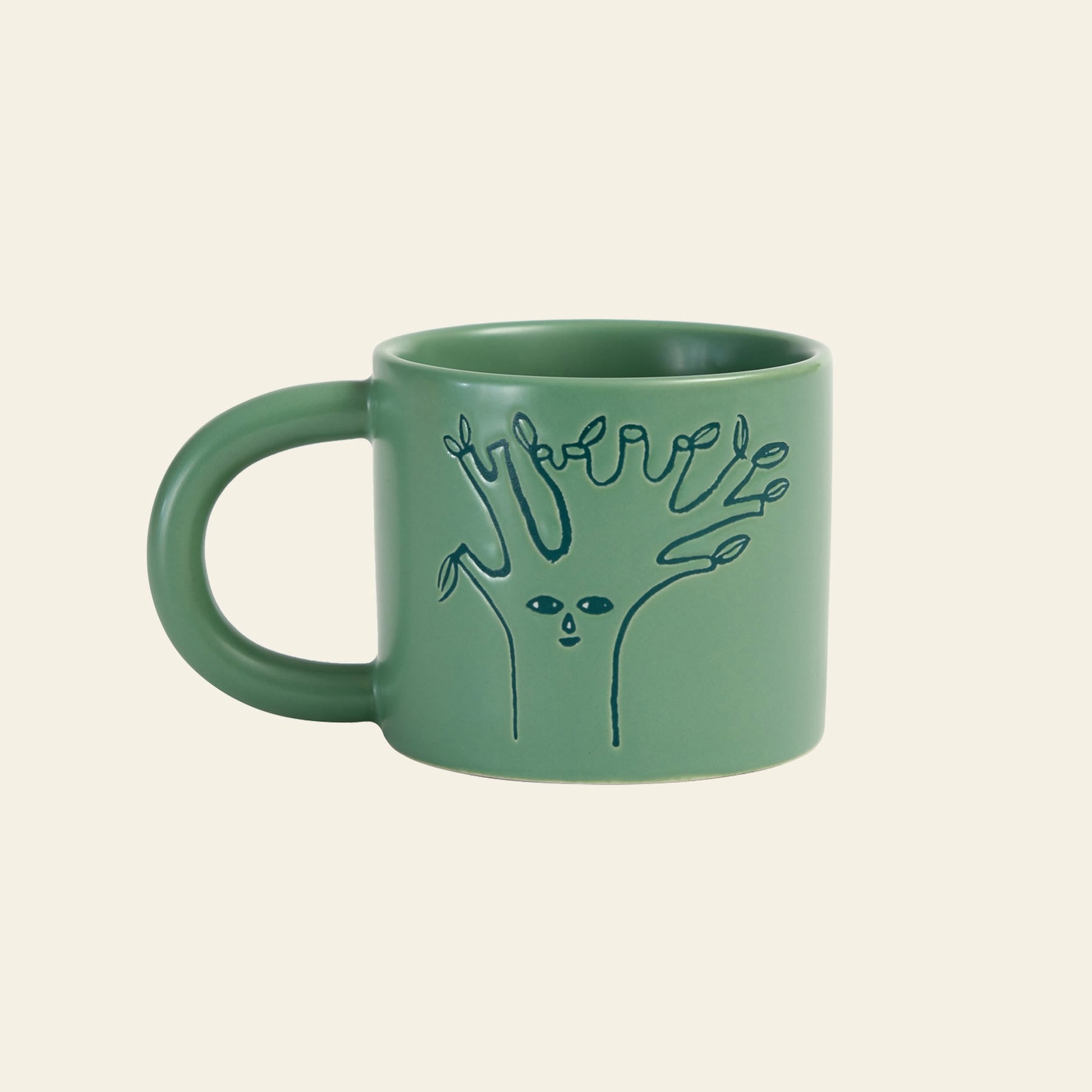 The Donna Wilson Tree Mug by Donna Wilson features a whimsical, line-drawn tree with a face and finger-like branches debossed on moss-green ceramic, creating a striking contrast against its off-white background.