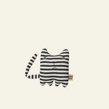 The Donna Wilson Wee One - Mono Kitten by Donna Wilson is a plush cat toy, hand-embroidered with black and white stripes, green eyes, straight mouth, and a striped tail. Made from organic cotton yarn. Suitable from birth. Shown on a beige background.