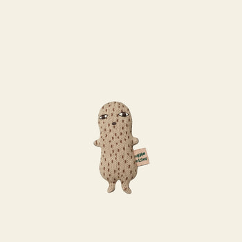 The Donna Wilson Wee One - Nutty by Donna Wilson is a small beige plush toy made from organic cotton, featuring dotted patterns, two arms, two legs, a neutral face, and a side tag. Stands upright against a plain background. Suitable from birth.
