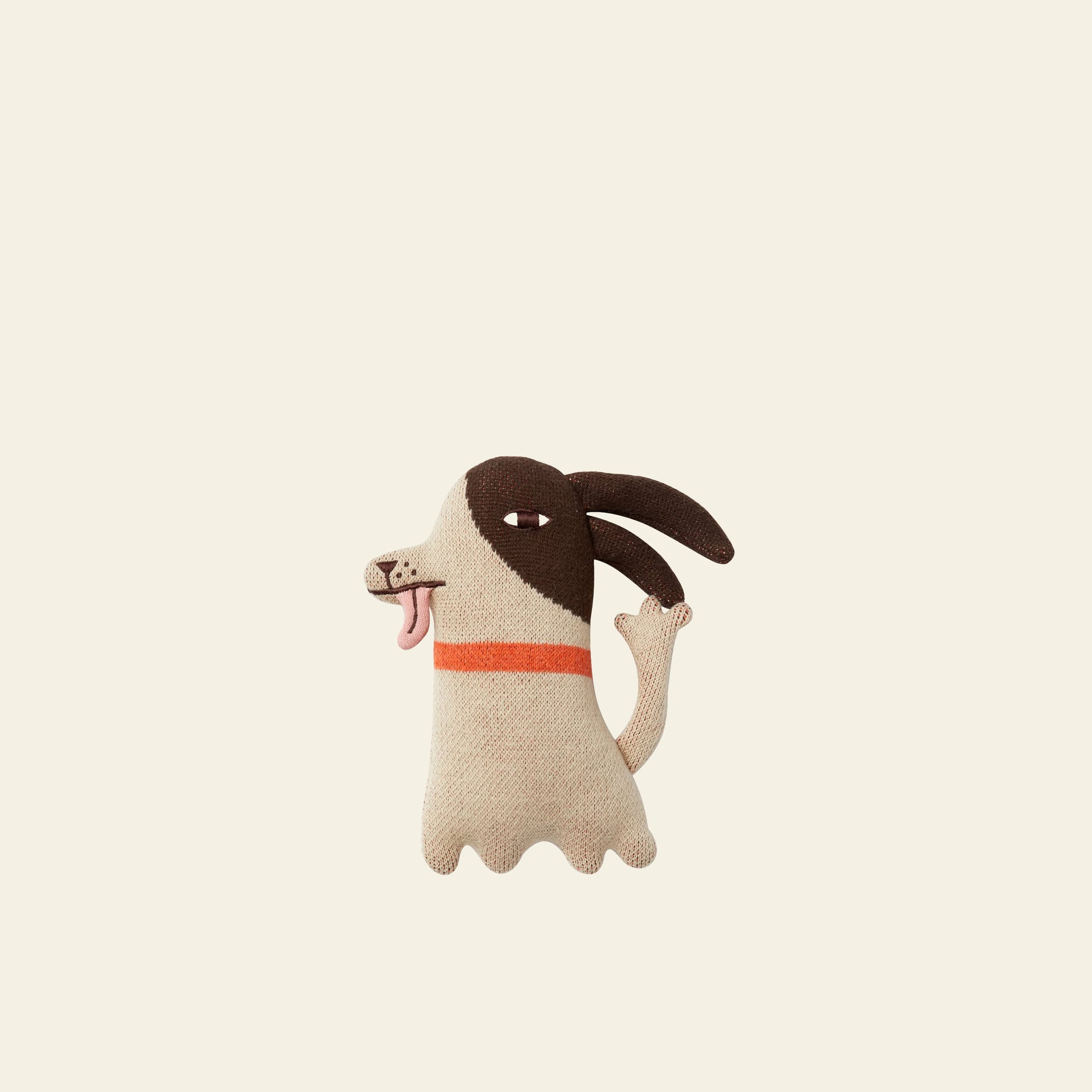 The Donna Wilson Wee One - Stanley Dog by Donna Wilson is a hand-embroidered, organic cotton stuffed toy featuring floppy dark brown ears, a beige body, pink tongue, mismatched eyes, and an orange neck stripe on a light background.