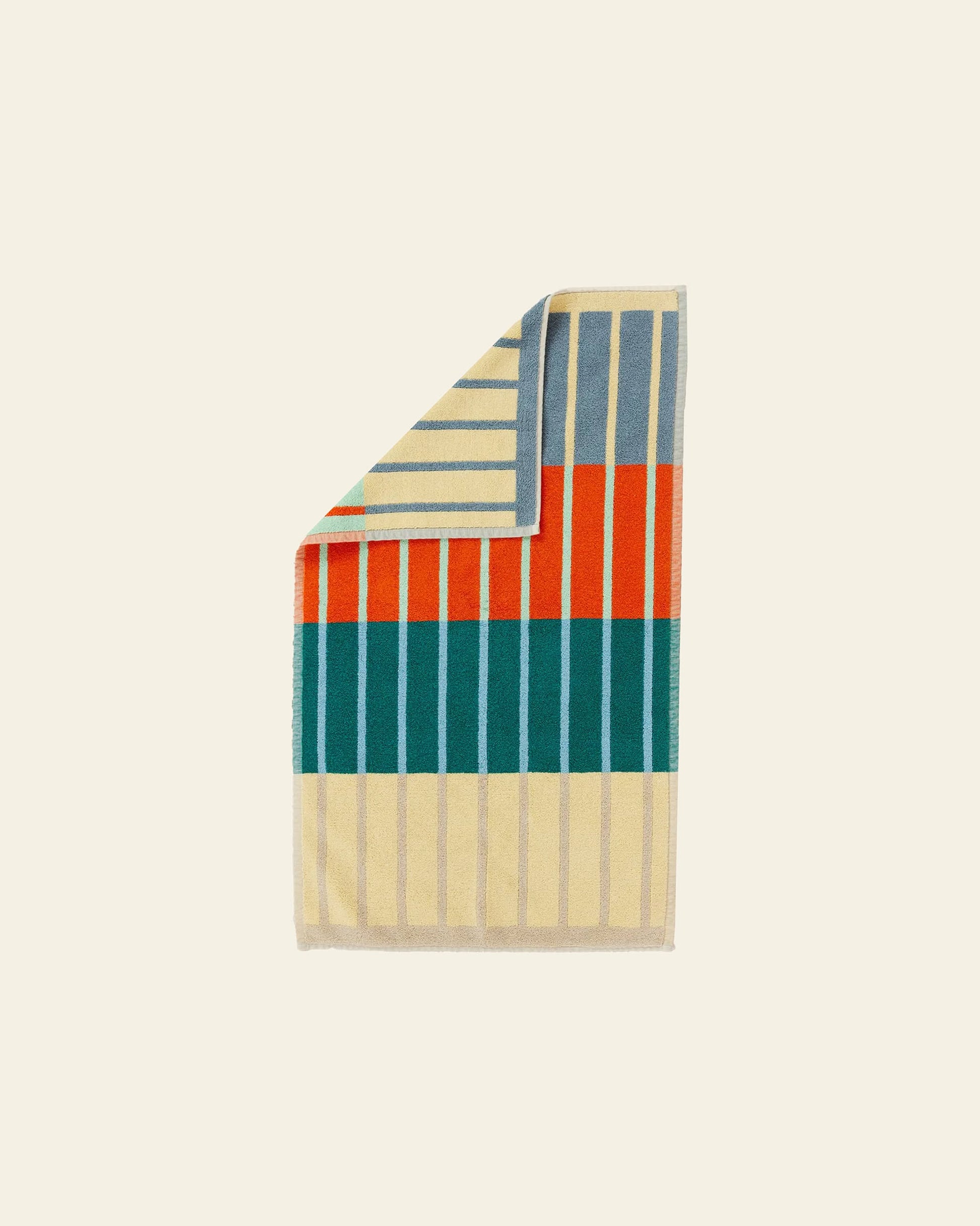 The Dusen Dusen House Stripe Concrete Bath Mat by Dusen Dusen features vertical beige, teal, orange, and blue stripes with a turned-down corner showing horizontal beige and blue stripes on the reverse. Set on a beige background. Oeko-Tex Standard 100 certified.