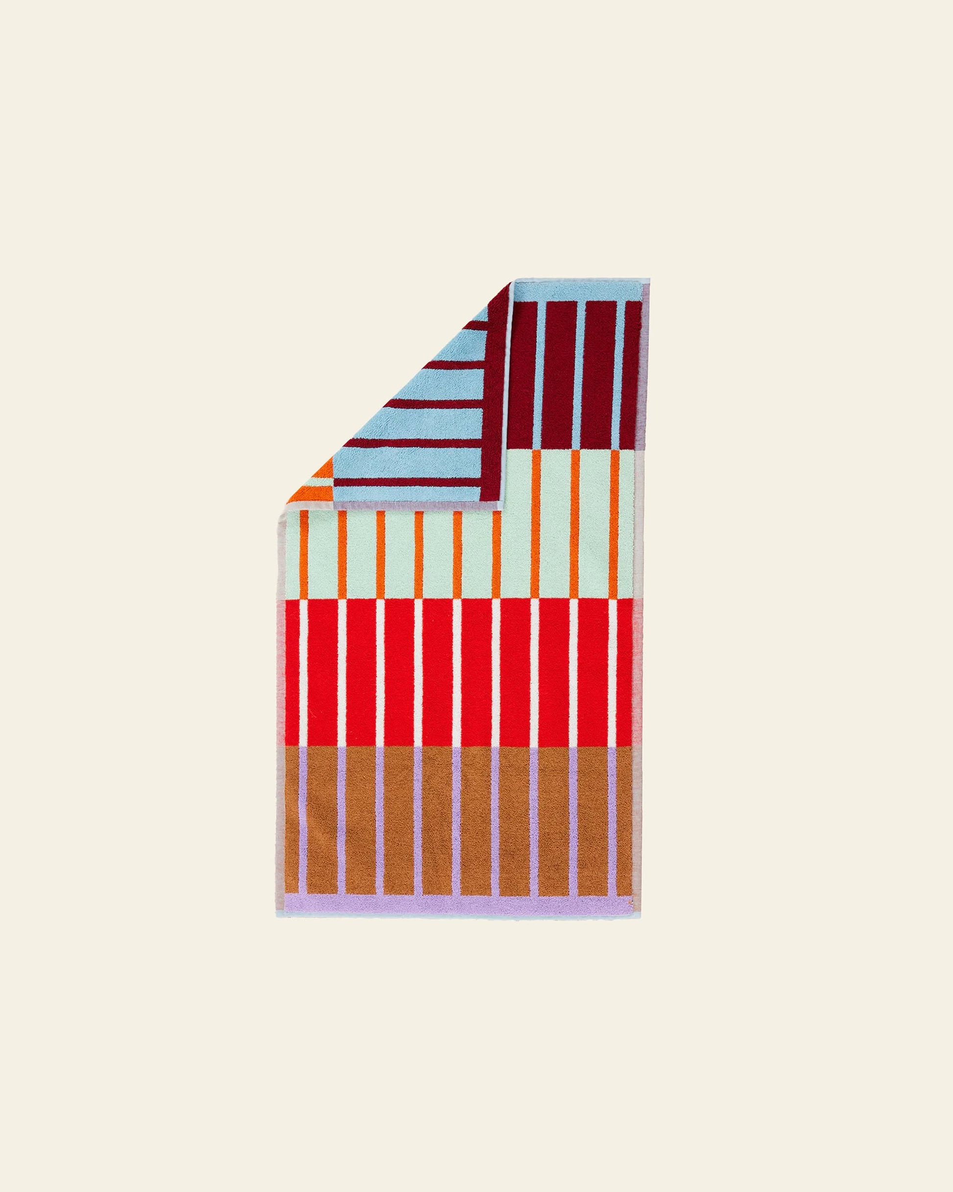 The Dusen Dusen House Stripe Copper Bath Mat features vibrant vertical stripes in brown, red, and light blue, plus a folded corner showing horizontal stripes in light blue, maroon, and orange—all made to Oeko-Tex Standard 100.
