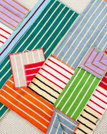 Dusen Dusens House Stripe Glass Hand Towel features absorbent, vibrant stripes in green, orange, blue, red, lavender, and cream, layered on a textured white surface for a bold geometric look.