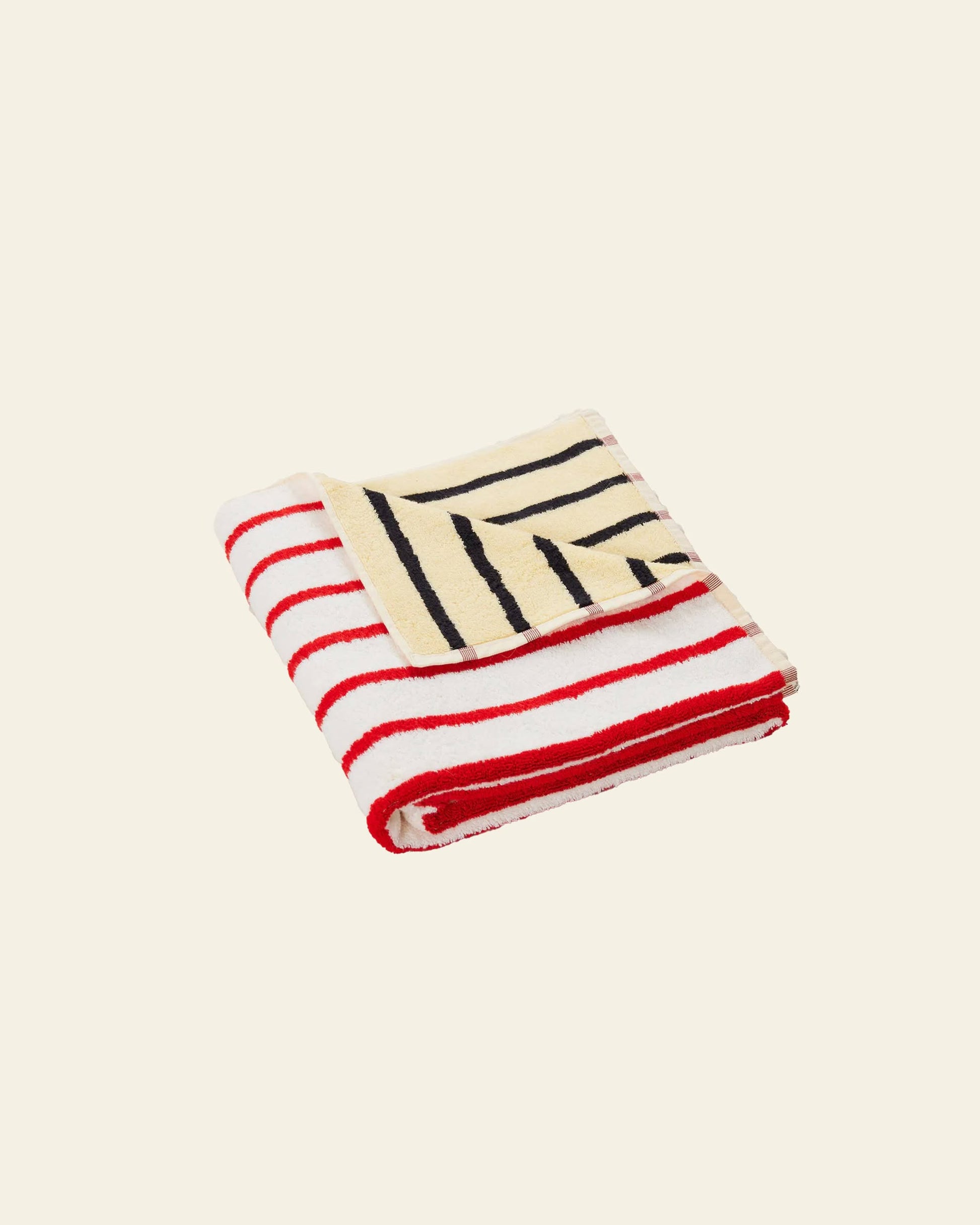 The Dusen Dusen House Stripe Stucco Bath Towel by Dusen Dusen features bold red and white horizontal stripes, a cream corner with black diagonal stripes, and is pictured on a plain light beige background.