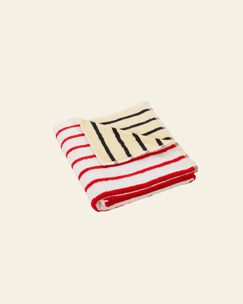 The Dusen Dusen House Stripe Stucco Bath Towel by Dusen Dusen features bold red and white horizontal stripes, a cream corner with black diagonal stripes, and is pictured on a plain light beige background.