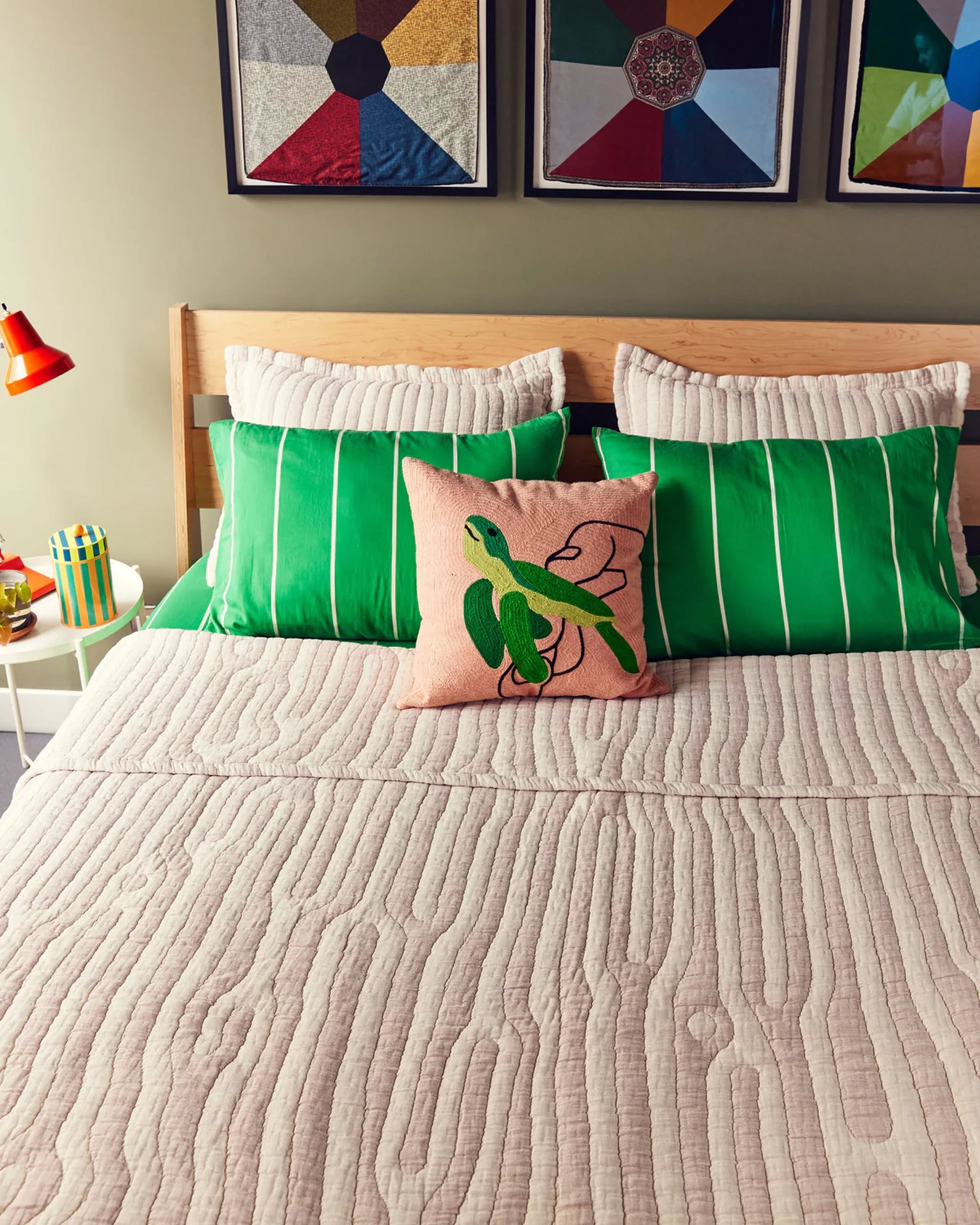 A neatly made bed features a beige quilt, two green-striped pillows, and the Dusen Dusen Turtle Pillow Cover by Dusen Dusen. Above, colorful geometric art adds a lively touch—perfect for fans of marine life decor.