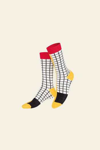 Add a playful touch to your look with Eat My Socks French Fries Socks by Eat My Socks—white socks with a black grid, yellow toes and heels, black soles, and red cuffs—quirky accessories shown on a light beige background.