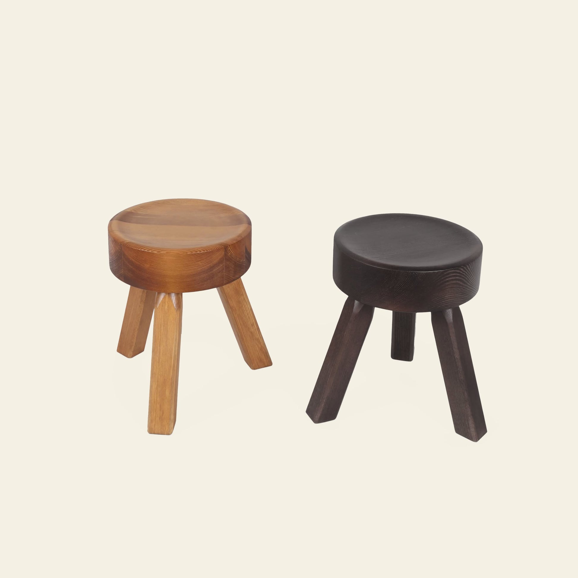 The FRAMA AML Stools by FRAMA are two small, solid oiled pine stools with round seats and three legs—one in light brown and one in dark brown—shown on a plain light background for versatile appeal.