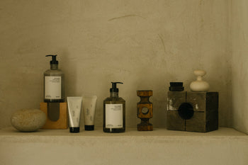 Minimalist display of FRAMA Hand Wash, 375ml, in pump bottles with organic ingredients. Arranged neatly with decorative objects on a beige shelf against a textured wall, featuring a neutral, earthy color palette.