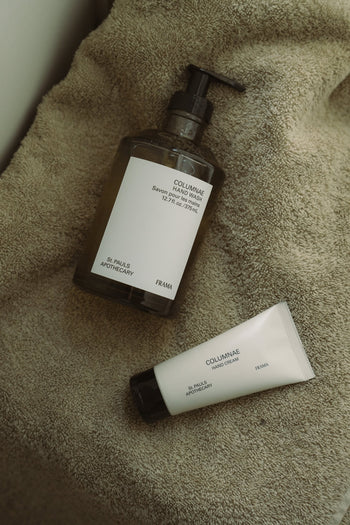 A bottle of FRAMA Hand Wash, 375ml, and a matching hand cream tube from FRAMA sit atop a soft beige towel.