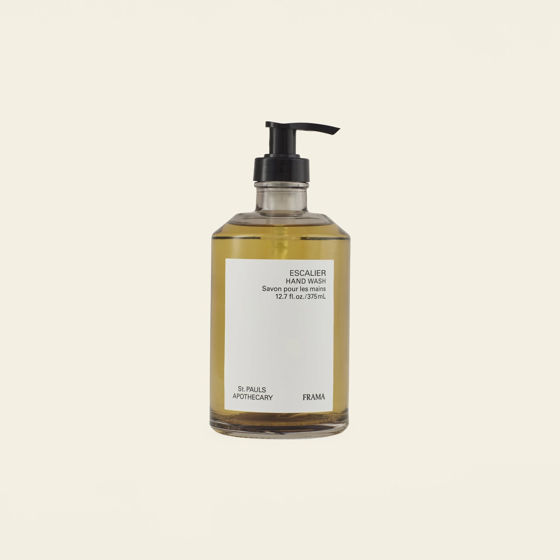 A clear pump bottle of FRAMA Hand Wash, 375ml, filled with yellow sandalwood liquid and made with organic ingredients, is set against a plain off-white background.