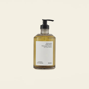 A clear pump bottle of FRAMA Hand Wash, 375ml, filled with yellow sandalwood liquid and made with organic ingredients, is set against a plain off-white background.